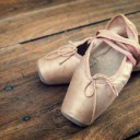 Old pink ballet shoes on a wooden floor, vintage process
